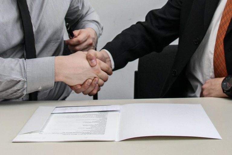 Hände schütteln über einem Tisch, auf dem ein Dokument liegt.